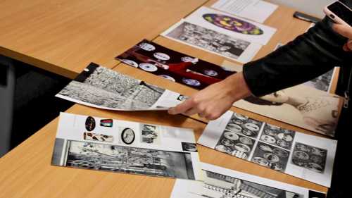 Image shows a curatorial activity with printed images of artworks on a table being arranged by hands coming in from the right