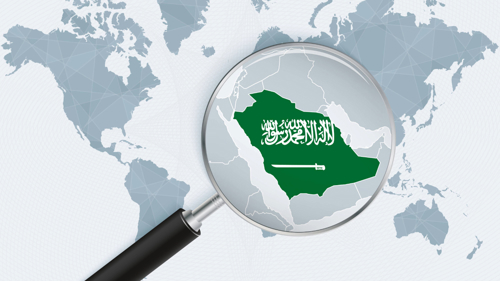 A graphic image showing a map of the world in two shades of grey to show land and ocean. Over the top of the Middle East is a magnifying glass, highlighting the outline of the country of Saudi Arabia which is filled in with the flag of the nation, a green background with white text and a sword on it